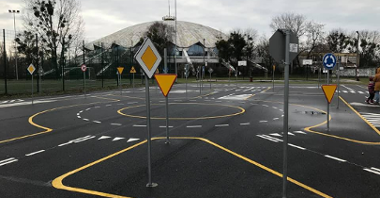 Rondo i znaki drogowe ustawione przy wjazdach na rondo w miasteczku rowerowym. W głębi Arena.