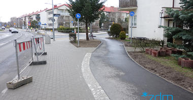 Na zdjęciu widać nowo wybudowaną drogę rowerową w terenie zabudowanym. Po jej jednej stronie wiidać jezdnię i chodnik, a po drugiej zabudowania wielorodzinne.