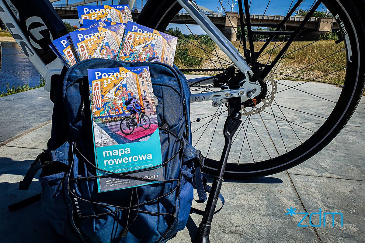 Na zdjęciu mapy rowerowe wystające z plecaka opartego o rower w okolicy mostu św. Rocha - grafika artykułu