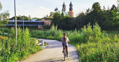 Zdjęcie rowerzystki jadące Wartostradą koło Bramy Poznania