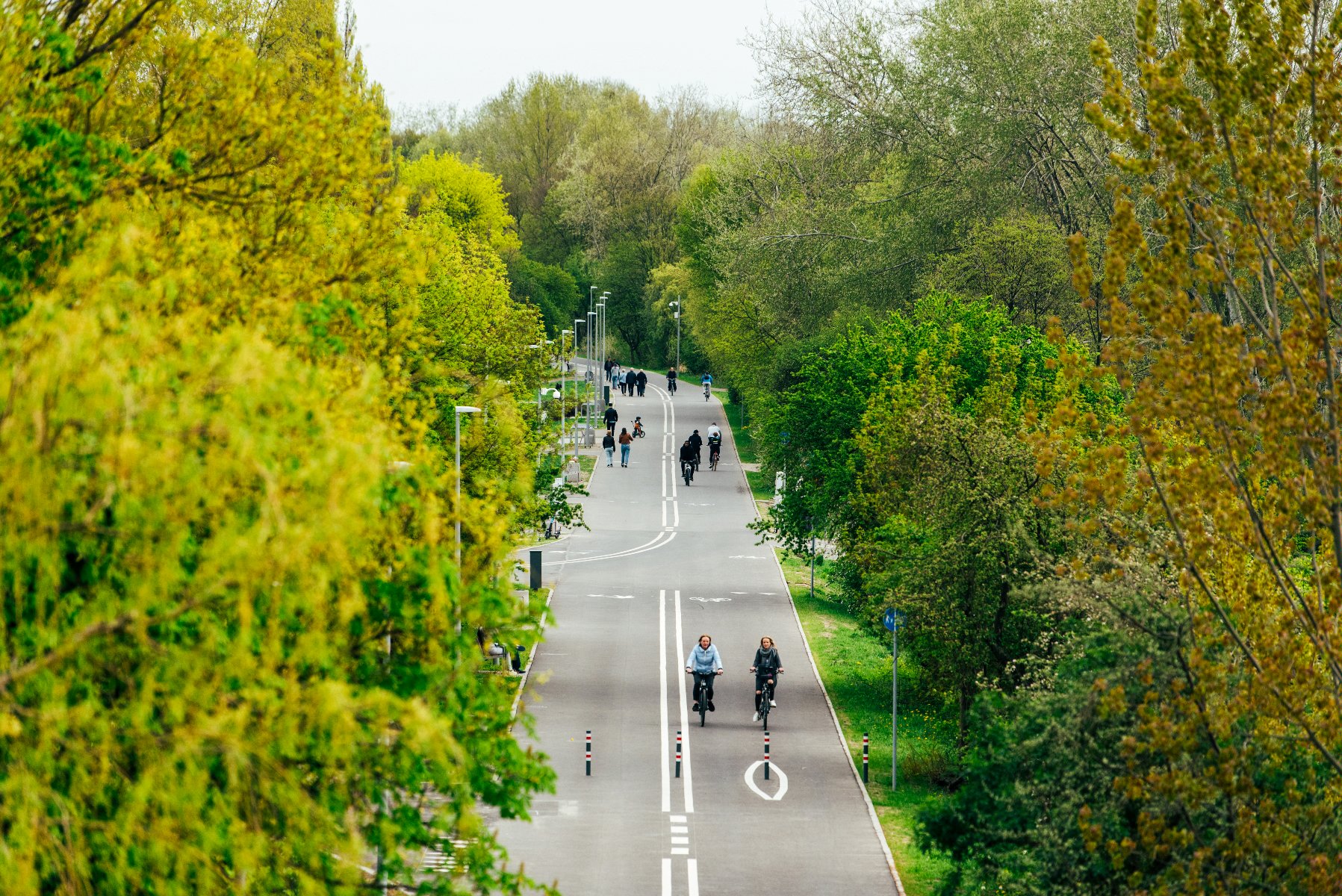 Zdjęcie przedstawia grupę ludzi jadących na rowererach lub przechadzających się po Wartostradzie. - grafika artykułu