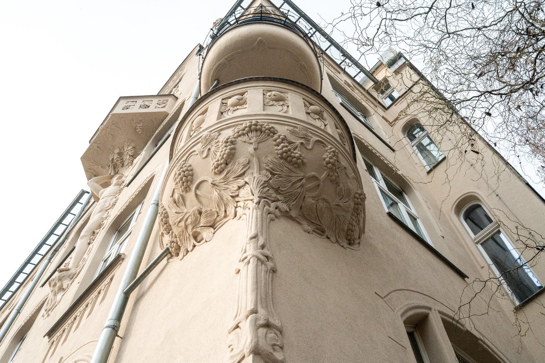 Wydarzenie poświęcone będzie wyzwaniom i możliwościom związanym z poprawą efektywności energetycznej budynków oraz transformacją zasobów budowlanych w Polsce Zewnętrzna fasada budynku z bogato zdobionymi detalami architektonicznymi. Na zaokrąglonym narożniku znajduje się ornamentyka, w tym motywy roślinne przypominające winorośl. Budynek ma kilka okien, a fotografia została wykonana z perspektywy patrzenia w górę.