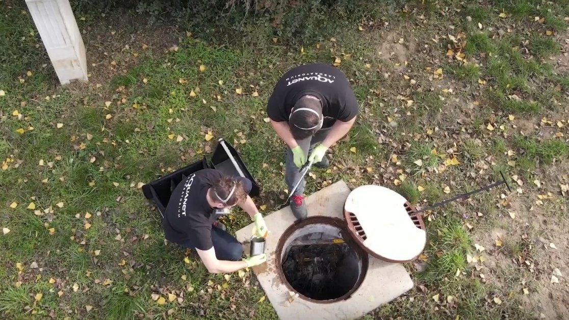 Na zdjęciu dwóch mężczyzn pobierających próbki z kanalizacji, widok z lotu ptaka