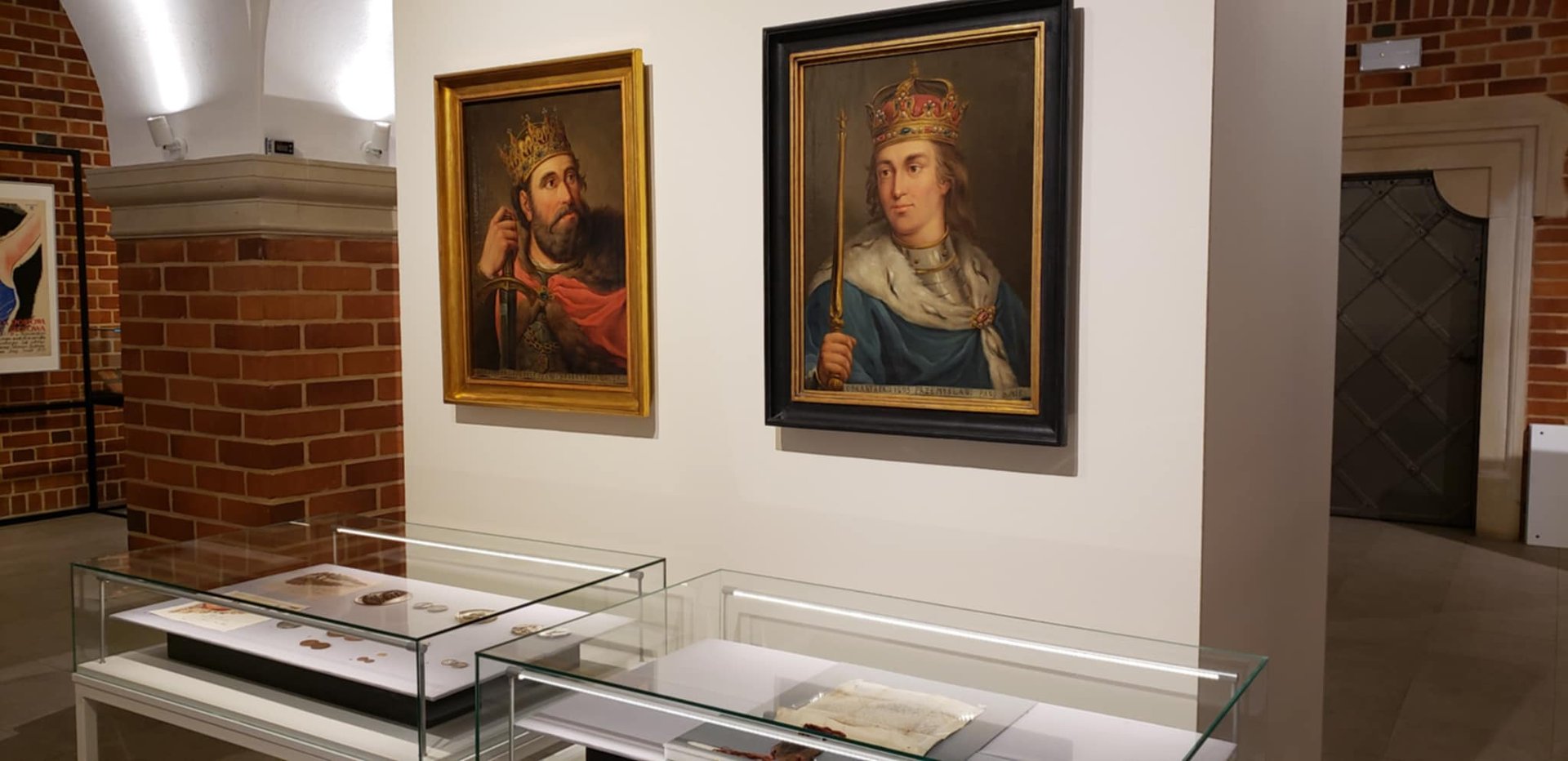 Bolesław Chrobry i Przemysł II, dokument z pieczęcią Przemysła, fot. Szymon Mazur Dwa obrazy i dwie gabloty w muzeum, na obrazach królowie, w gablocie monety, dokument