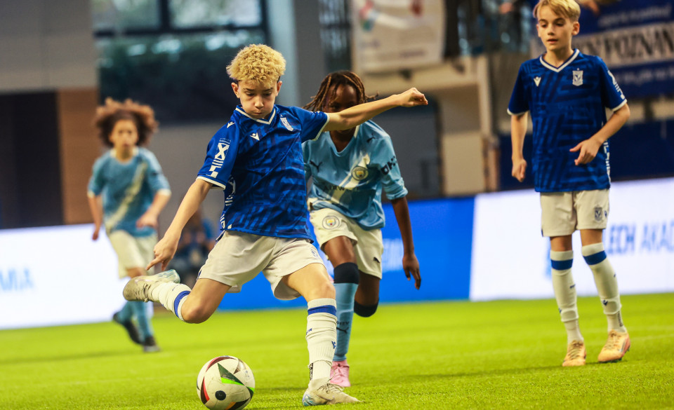 Enea Lech Cup 2025, fot. Adam Jastrzębowski - zawodnik w niebieskiej koszulce i białych spodenkach oddaje strzał. W tle widać jego jednego kolegę z drużyny oraz dwóch zawodników przeciwnego zespołu w błękitnych koszulkach i białych spodenkach