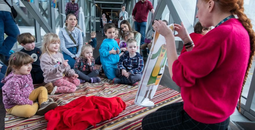 Spotkanie Niezwykłe przygody odważnego króla należy do cyklu Magiczny dywan w Bramie Poznania Grupa dzieci z zainteresowaniem obserwuje animatorkę, która trzyma w dłoniach obrazek króla. Dzieci siedzą z "magiczny dywanie".