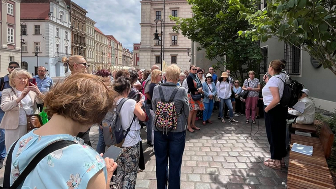 Grupa osób na Starym Rynku słucha przewodnika.