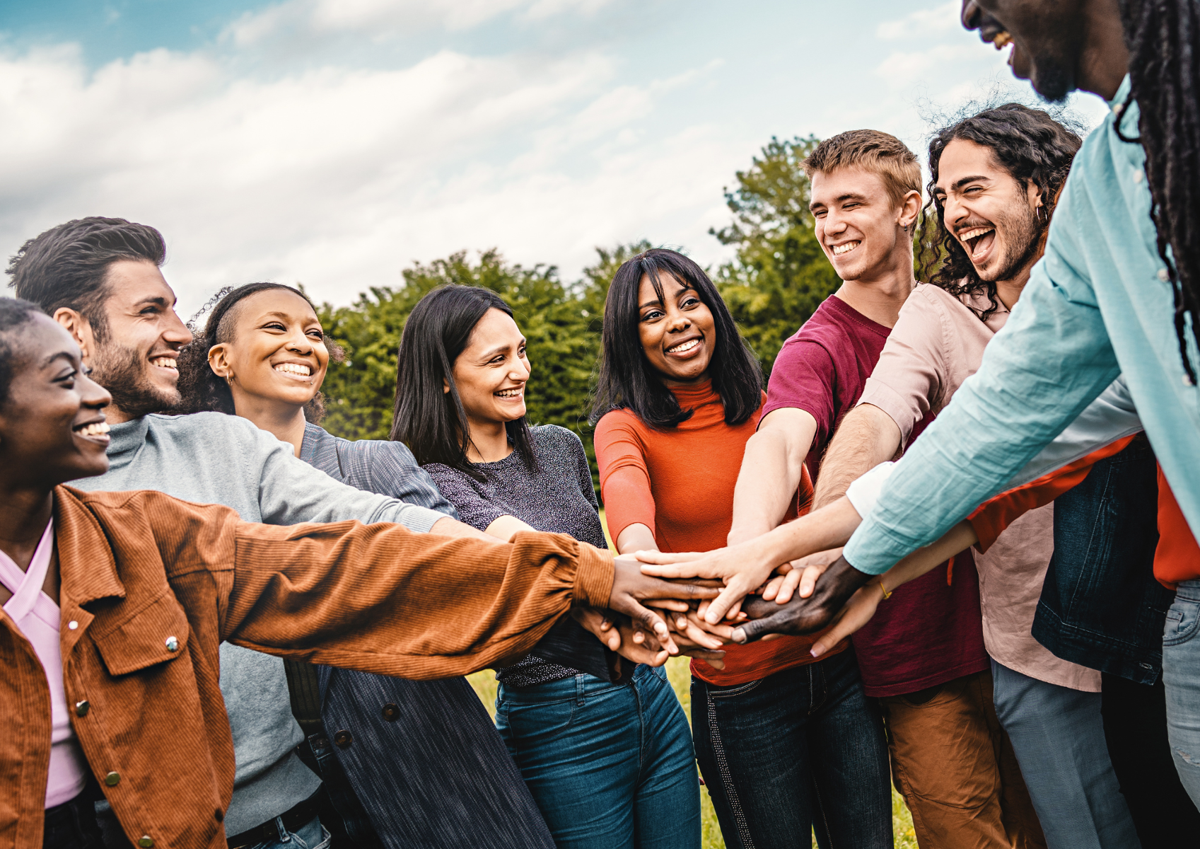 Grupa osób o różnym kolorze skóry stoi w okręgu, kładąc na sobie ręce skierowane do środka koła.
