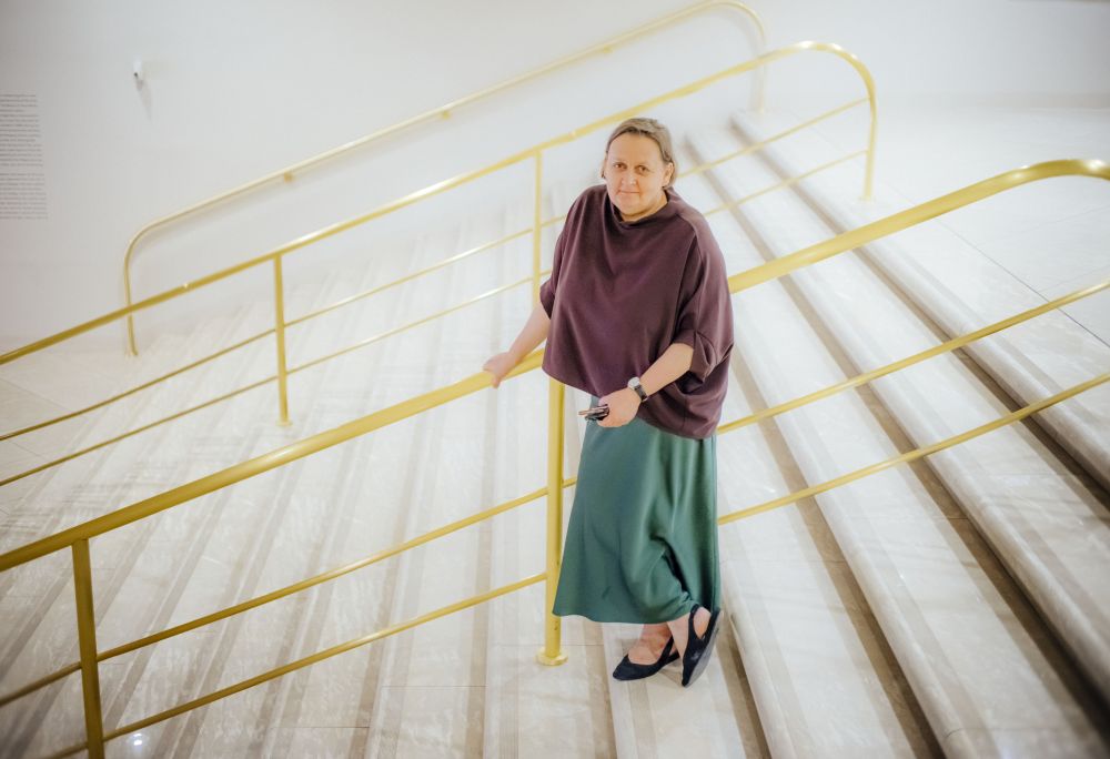 Kobieta stoi na schodach ze złotymi poręczami patrząc w górę.