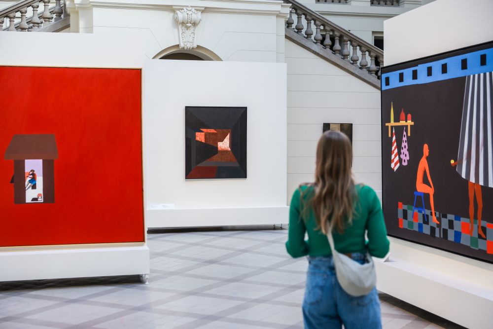 Kobieta stojąca tyłem do obiektywu ogląda obrazy wiszące na ścianach.