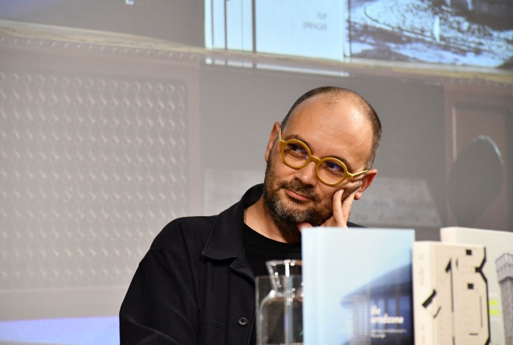 Mężczyzna w okularach podpiera głowę ręką.