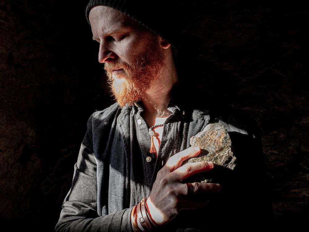 Muzyk ma rudą brodę, na głowie czapkę. Stoi na scenie, śpiewając i jednocześnie grając na klawiszach.