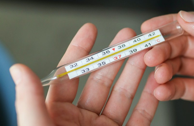 Na zdjęciu dłonie trzymające termometr rtęciowy