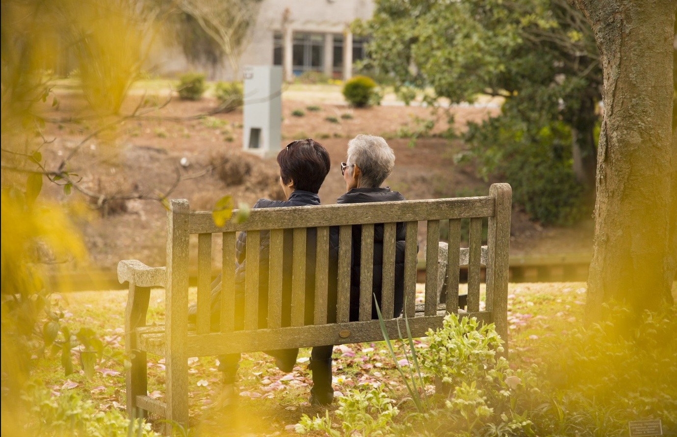 Na zdjęciu dwie seniorki siedzące na ławce w parku