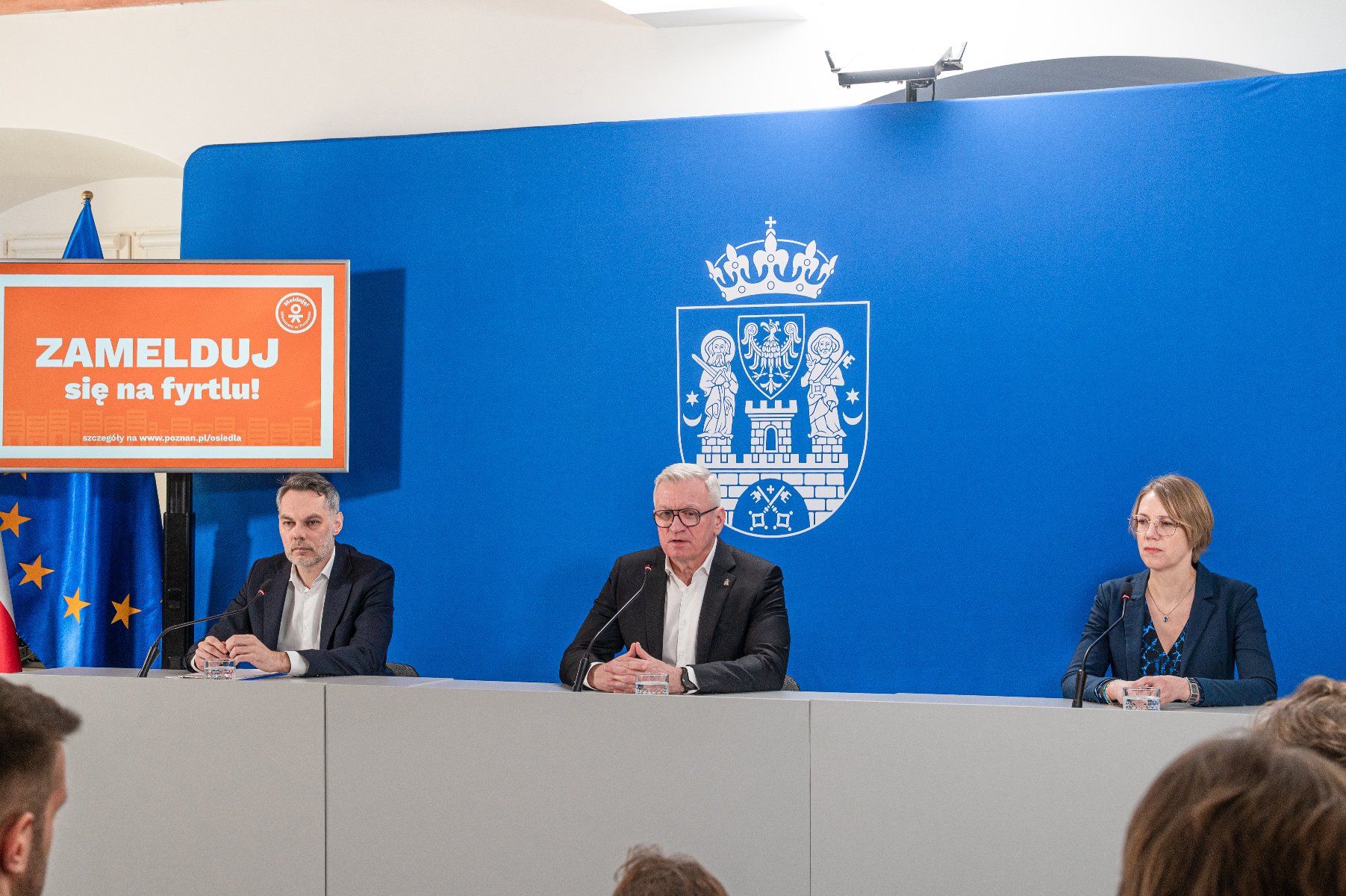 Zakończenie konkursu nastąpi 31 grudnia 2025 r. Na zdjęciu dwóch mężczyzn i kobieta za stołem konferencyjnym, w tle niebieska ścianka z herbem miasta