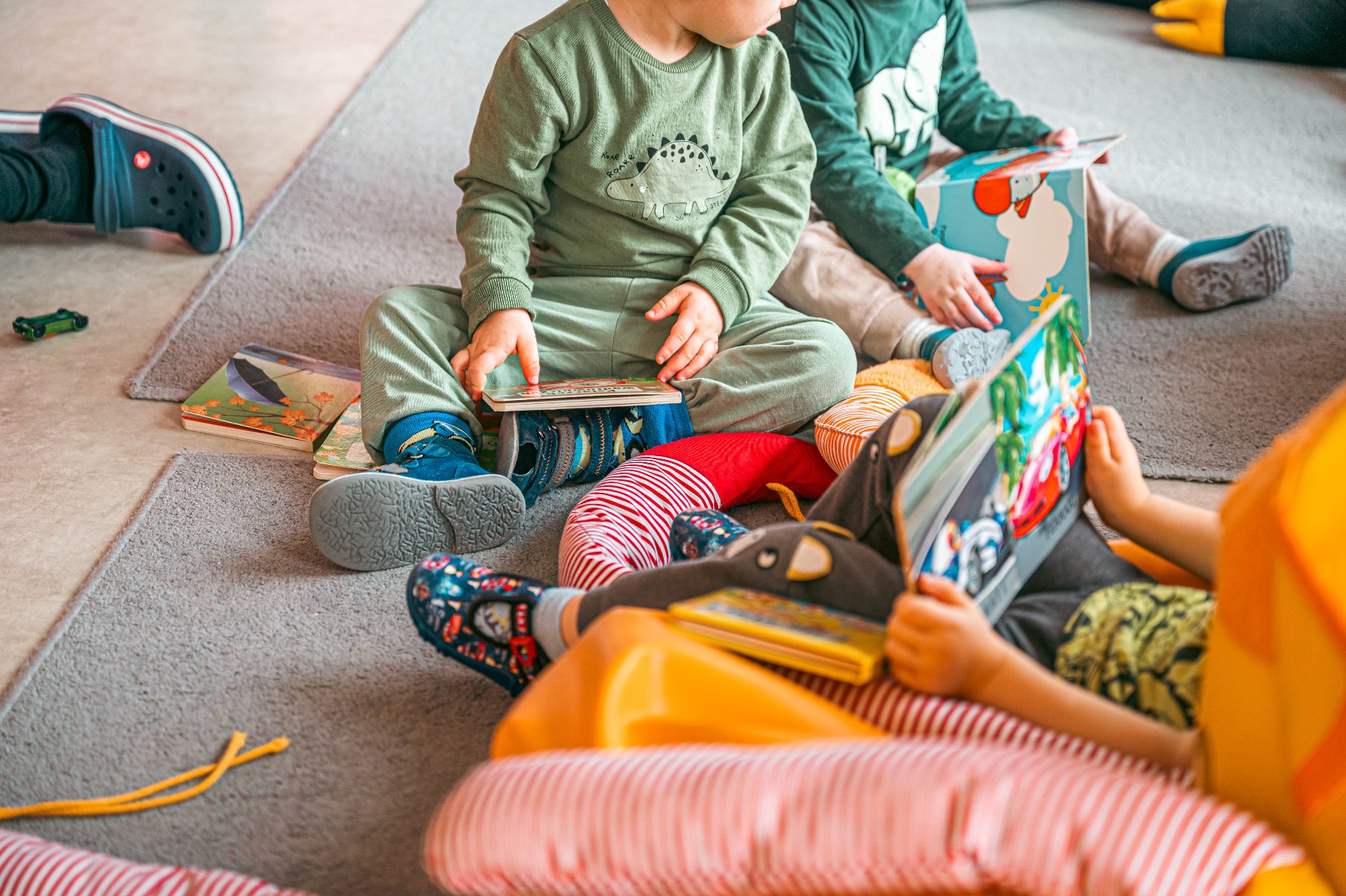 Na zdjęciu dzieci bawiące się książkami na dywanie, nie widać ich twarzy