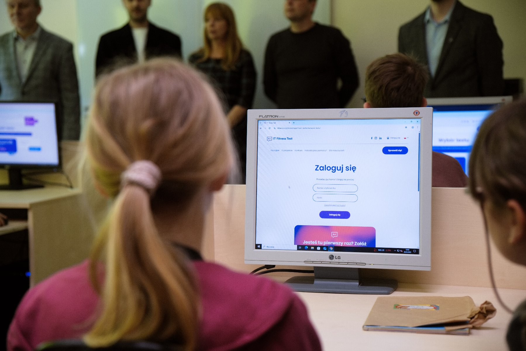 Na zdjęciu dziewczynka siedząca przed komputerem, na ekranie napis: zaloguj się