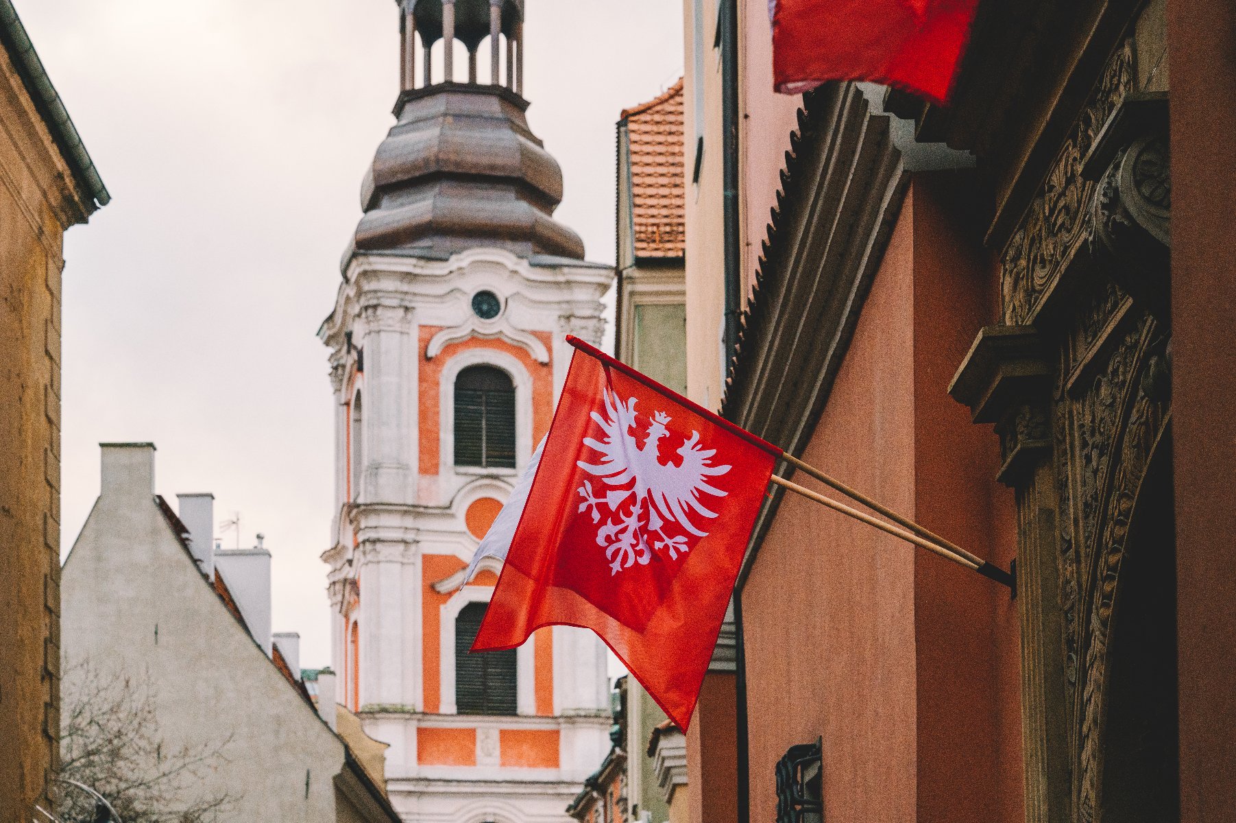 Na zdjęciu flaga powstańcza zawieszona na kamienicy, w tle wieża kościoła farnego