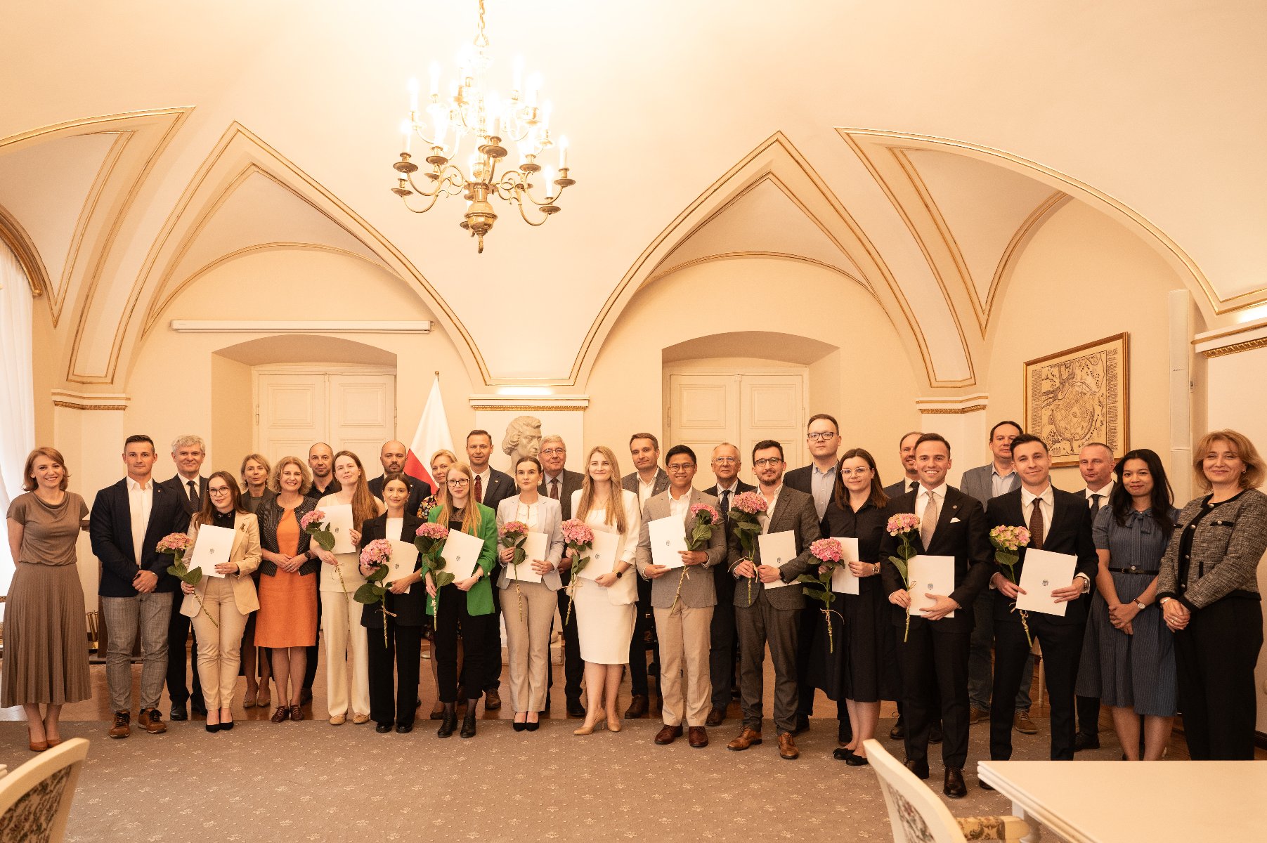 Stypendium dla młodych badaczy na zdjęciu grupa osób trzymających dyplomy i kwiaty