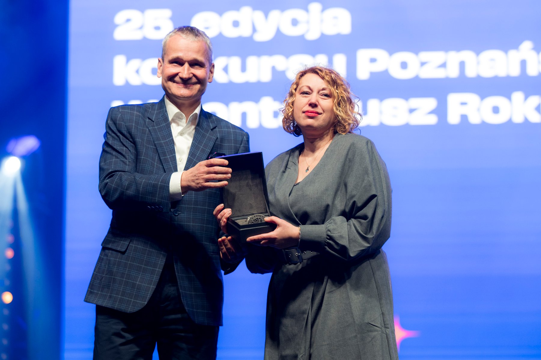 Na zdjęciu kobieta trzymająca kwiaty mówi coś do mikrofonu