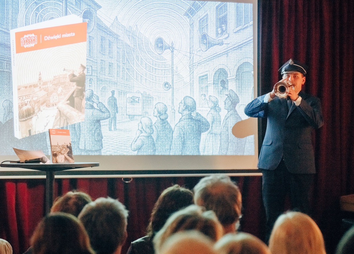 na zdjęciu mężczyna w mundurze grający na trąbce przed widownią, za nim na dużym ekranie wyświetlana jest prezentacja multimedialna - więcej w treści artykułu