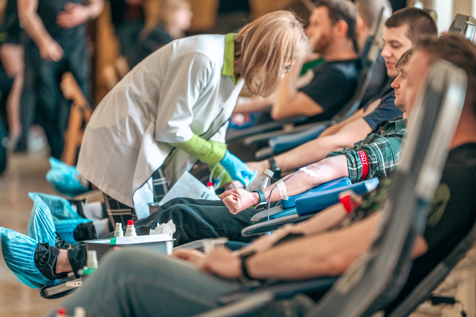 Na zdjęciu pielęgniarka pochylona nad mężczyzną, który oodaje krew, w tle dużo innych osób