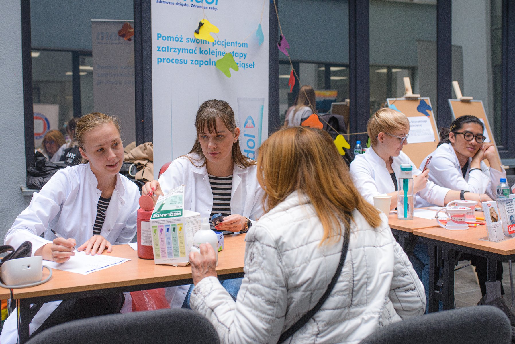 Na zdjęciu stoisko, przy nim trzy kobiety, dwie z nich noszą lekarskie fartuchy