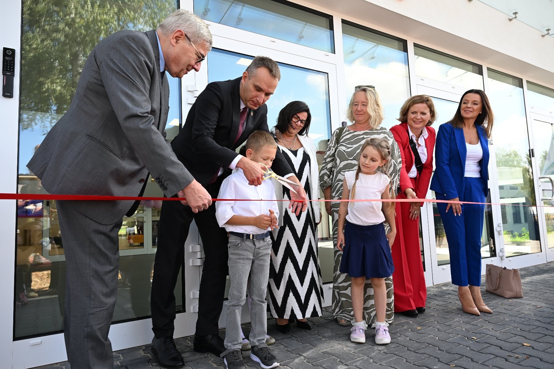 Zdjęcie przedstawia dzieci i dorosłych podczas przecinania wstęgi. - grafika artykułu