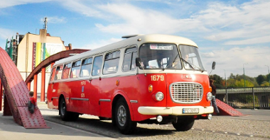 Zdjęcie przedstawia czerwony zabytkowy autobus, jadący po moście Jordana.
