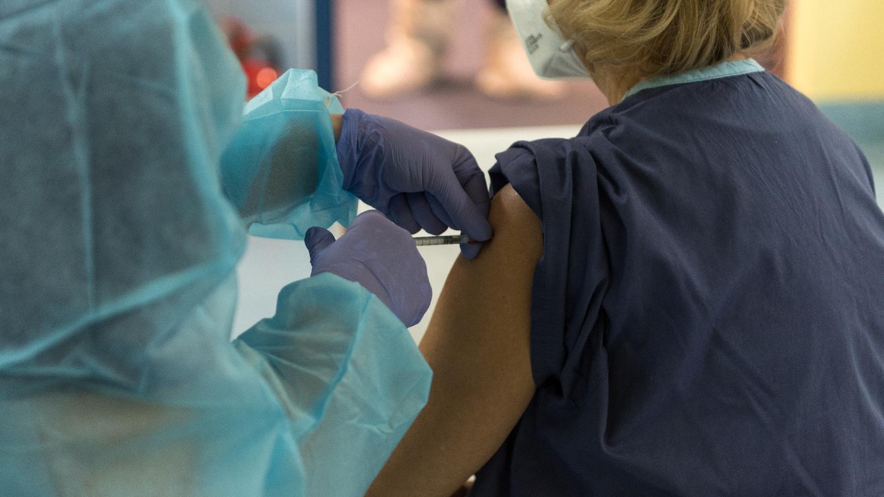 Na zdjęciu szczepienie: osoba w medycznym stroju szczepi kobietę; nie widać ich twarzy, w centrum zdjęcia dłonie ze szczepionką - grafika artykułu