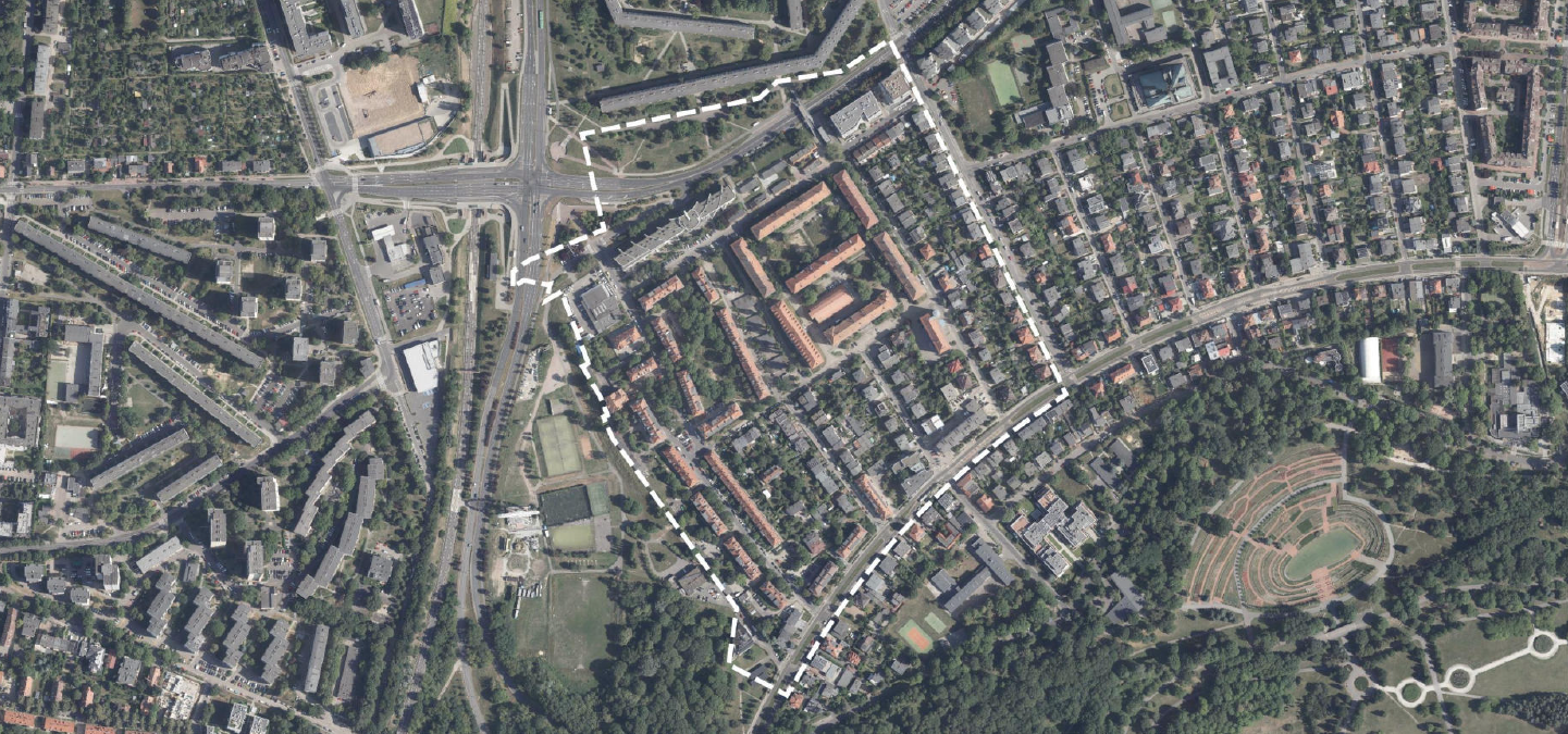 Widok z lotu ptaka na miejską przestrzeń. Obrazek ukazuje szczegółowy układ budynków, ulic i terenów zielonych. W centralnej górnej części krzyżuje się kilka głównych dróg, tworząc skomplikowaną siatkę ulic. W prawym dolnym rogu widoczny jest duży obszar zieleni z amfiteatrem lub okrągłą strukturą z tarasowymi siedzeniami. Zdjęcie oddaje zróżnicowanie funkcji miejskich - mieszkalnych, komercyjnych i rekreacyjnych. - grafika artykułu