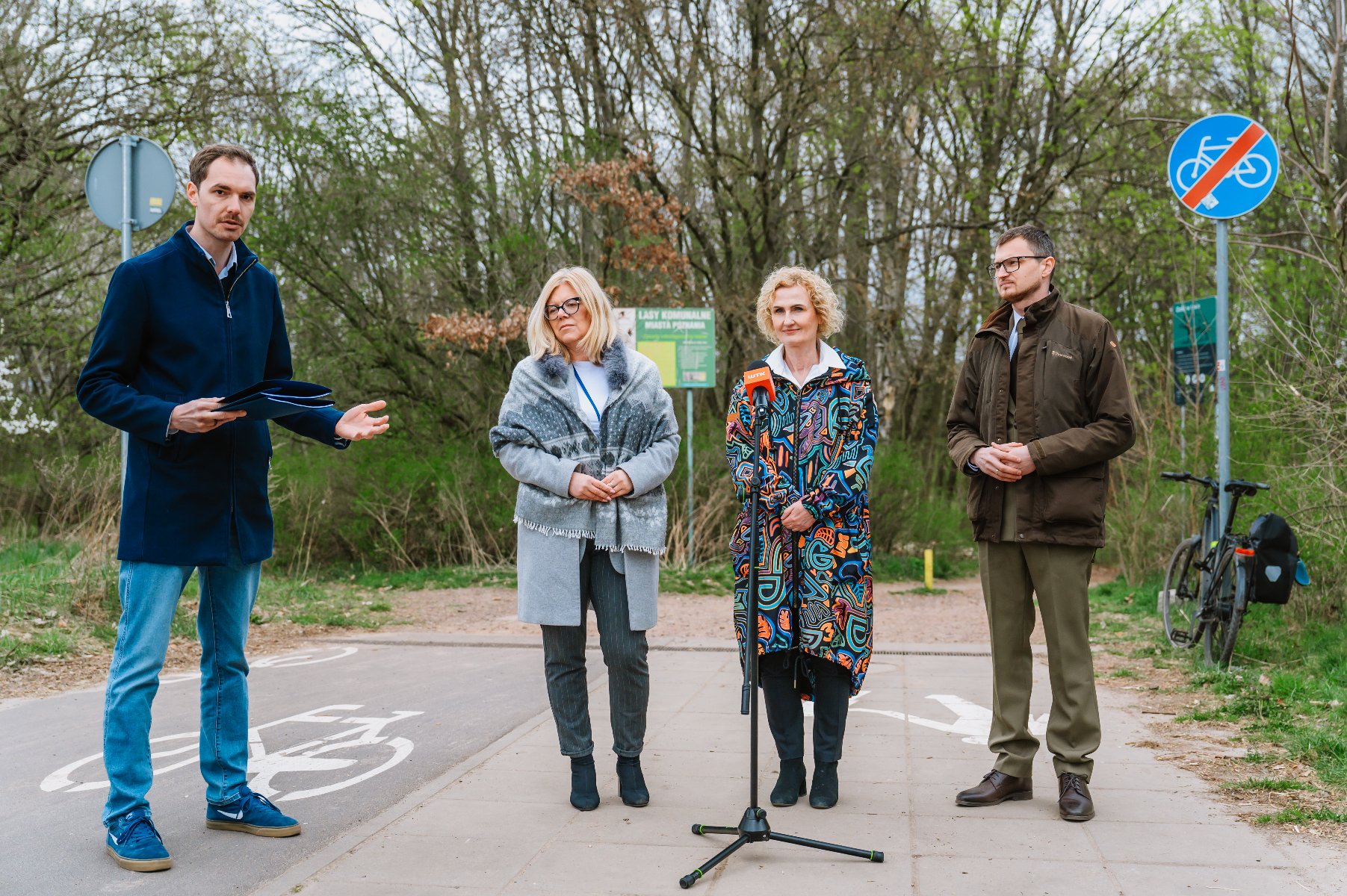 Zdjęcie przedstawia uczestników konferencji prasowej - dwie kobiety i dwóch mężczyzn stojących na ścieżce pieszorowerowej. Za ich plecami znajduje się las. - grafika artykułu