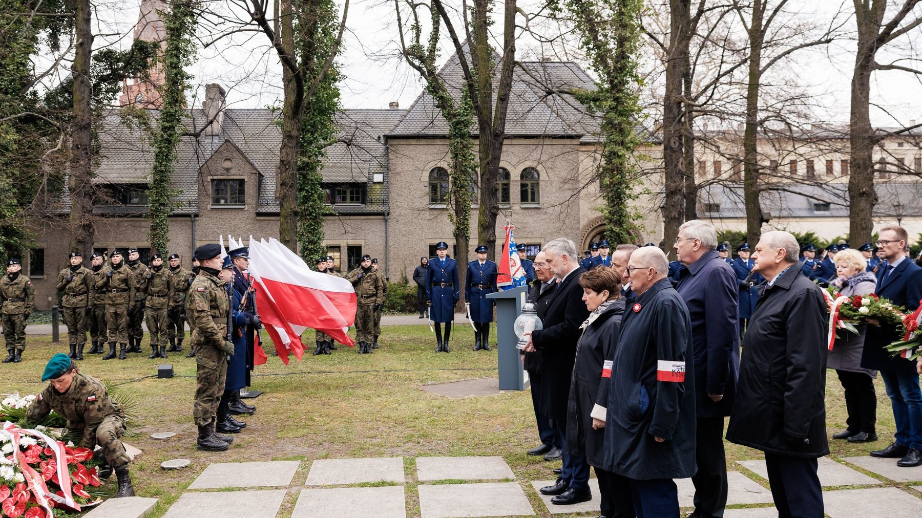 Na zdjęciu delegacja składająca kwiaty pod pomnikiem, w tle asysta wojska i innych mundurowych