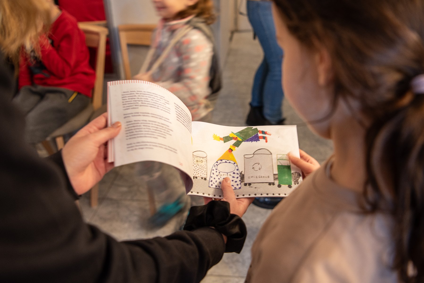 Na zdjeciu dwie osoby, w tym mała dziewczynka, czytające kolorową książkę - grafika artykułu