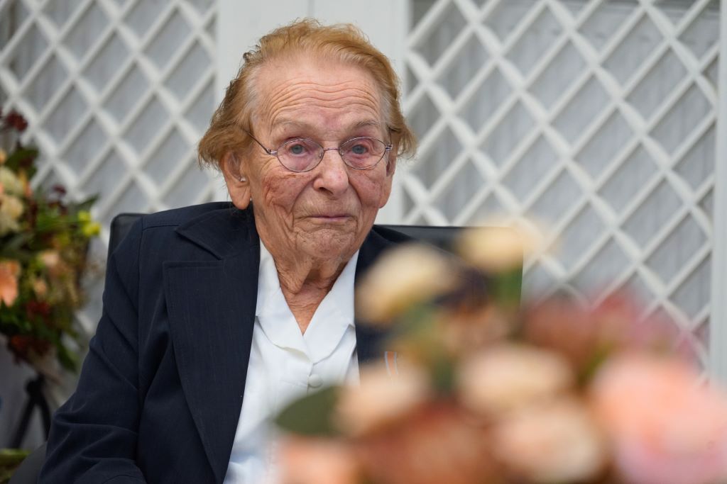 Na zdjęciu starsza pani, obok, na pierwszym planie, kwiaty - grafika artykułu