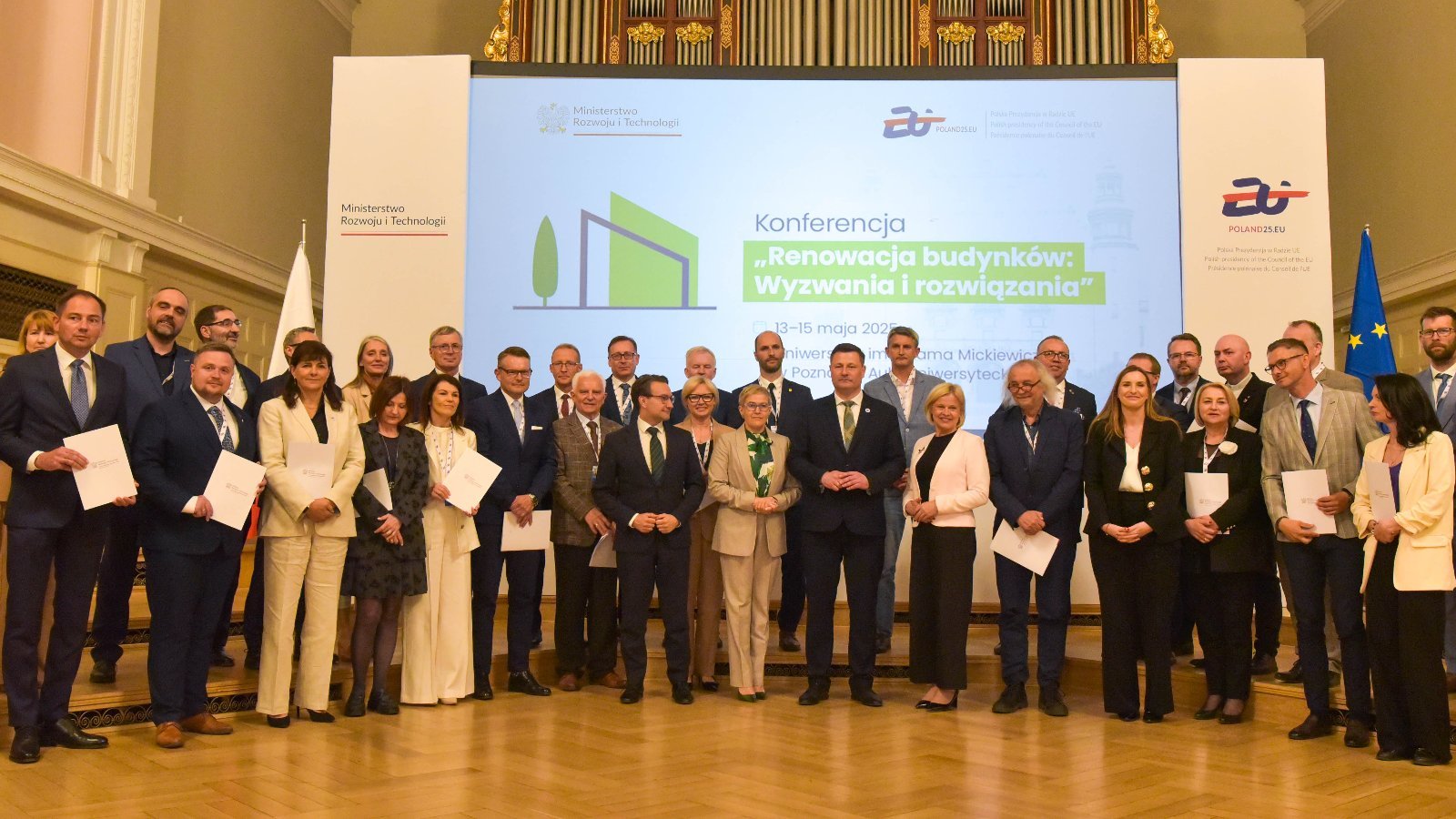 Grupa osób stoi na scenie podczas uroczystego wydarzenia, prawdopodobnie konferencji lub gali wręczenia nagród.