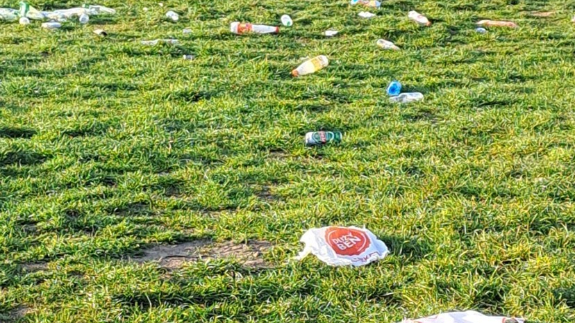 Zdjęcie przedstawia leżące na trawie śmieci, głównie butelki i puszki.