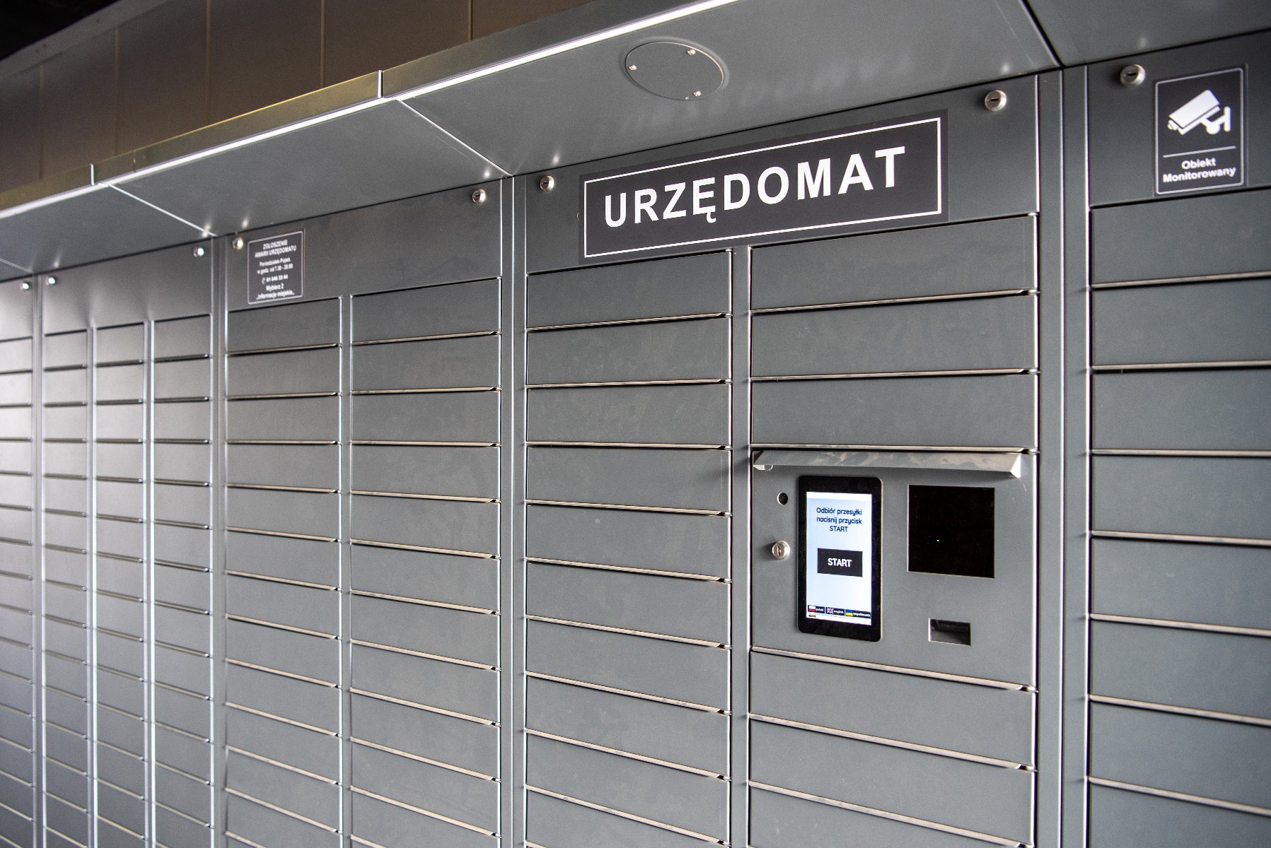 Zdjęcie przedstawia szarą maszynę z napisem "Urzędomat". Przypomina ona urządzenie z paczkami. - grafika artykułu