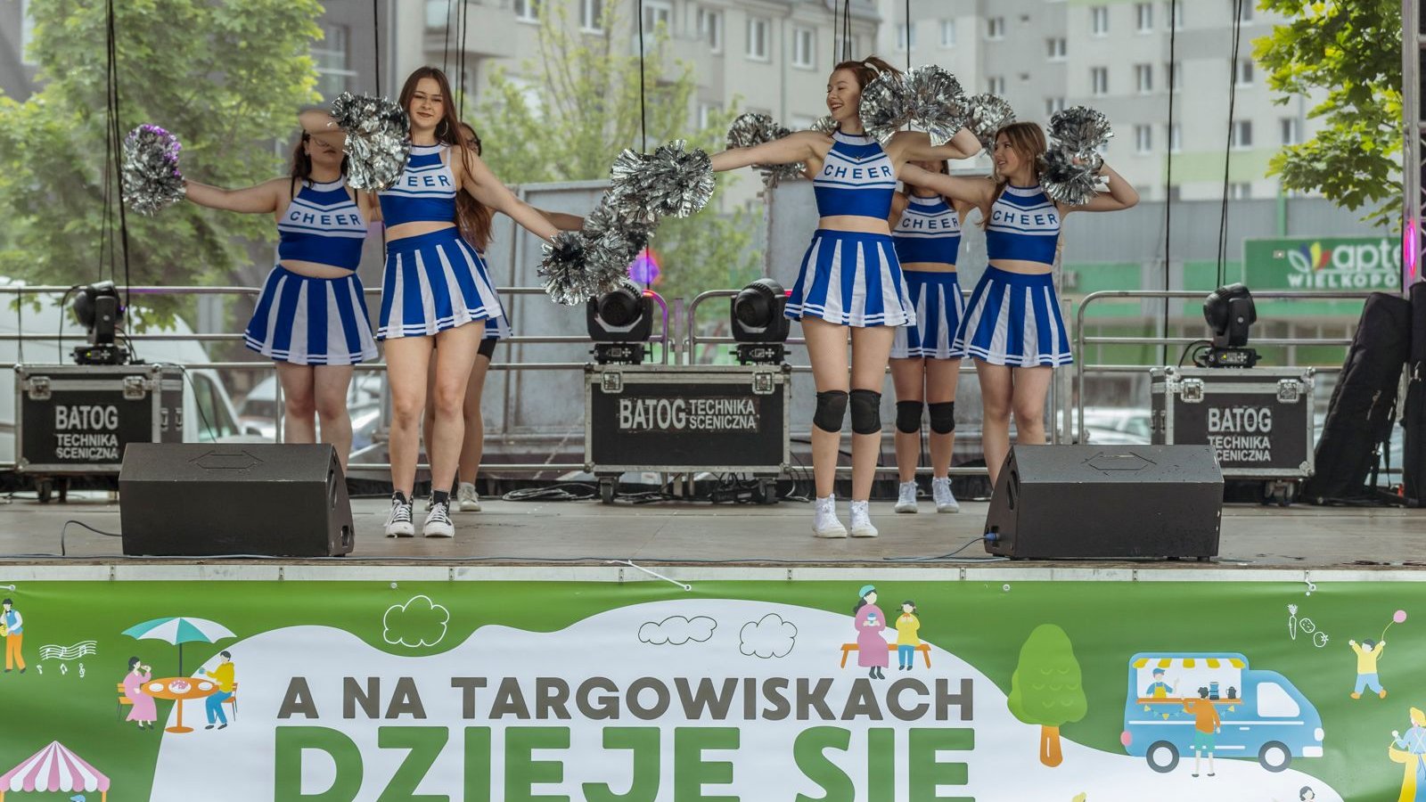 Zdjęcie przedstawia grupę dziewczyn tańczących na scenie z pomponami w rękach.