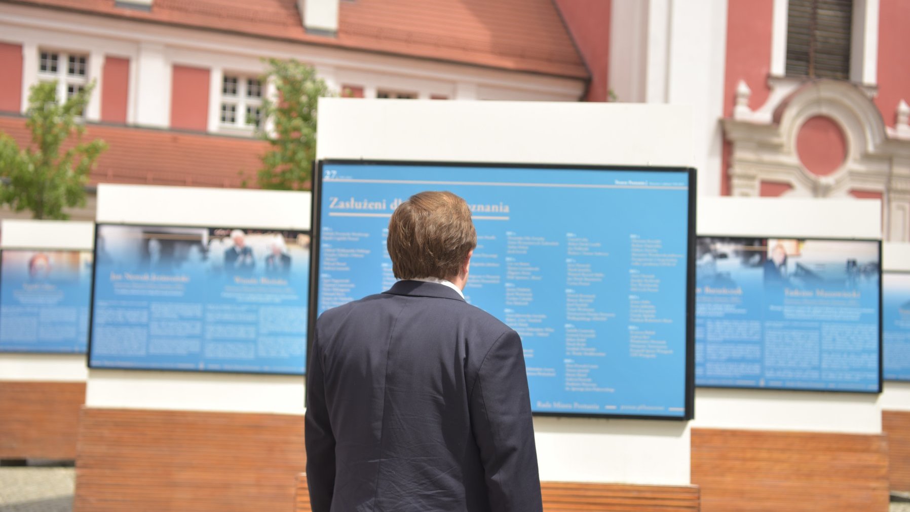 Zdjęcie przedstawia fragment wystawy i oglądającego ją mężczyznę. Stoi on tyłem do aparatu.