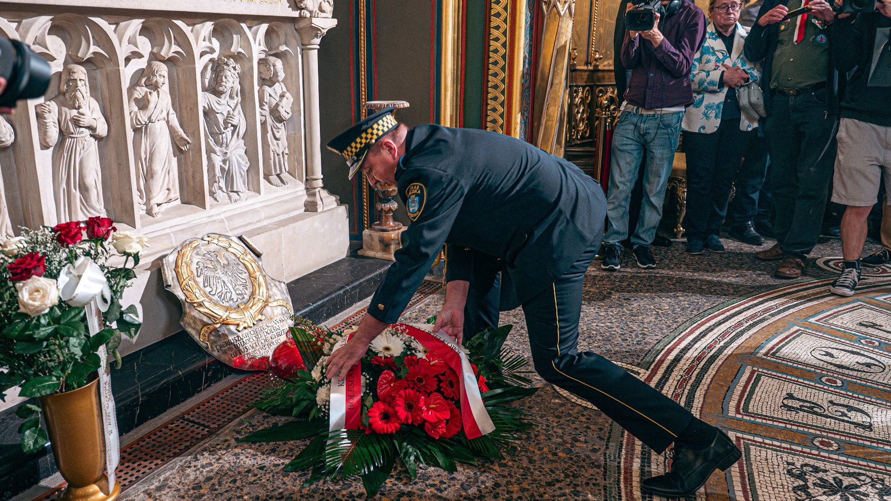 Zdjęcie przedstawia strażnika miejskiego kładącego bukiet kwiatów przed sarkofagiem.
