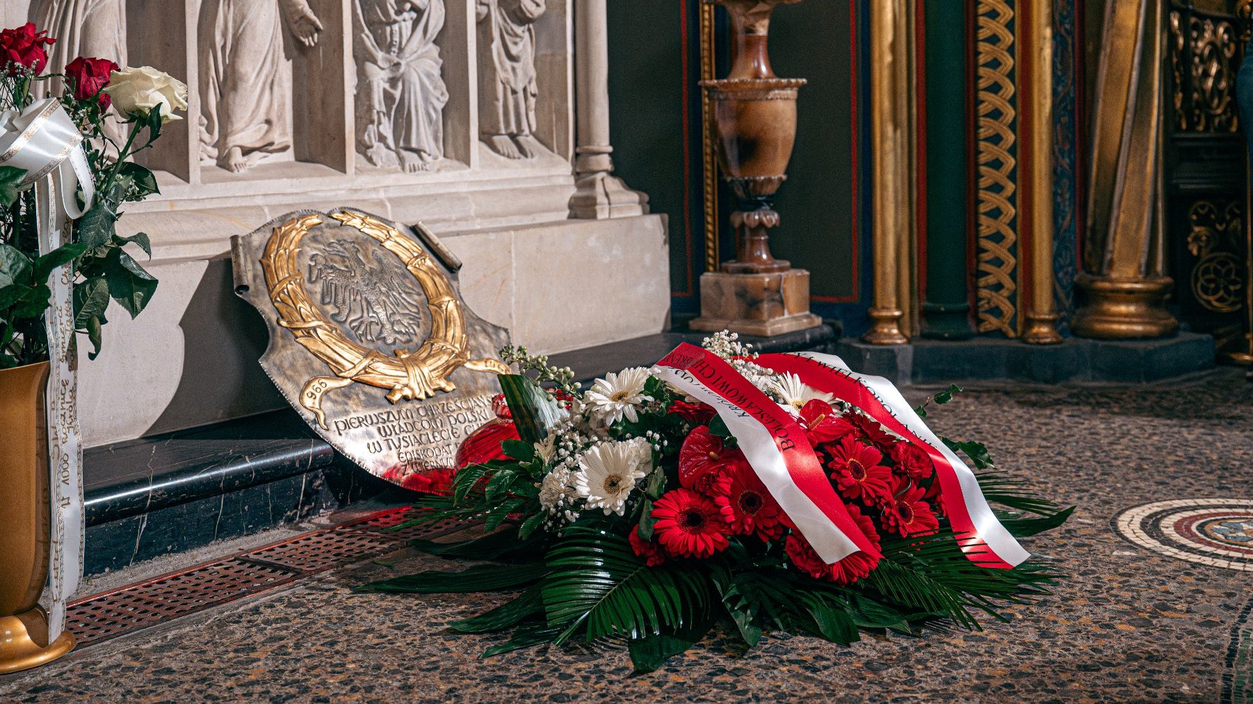 Zdjęcie przedstawia bukiet kwiatów leżących przed sarkofagiem.