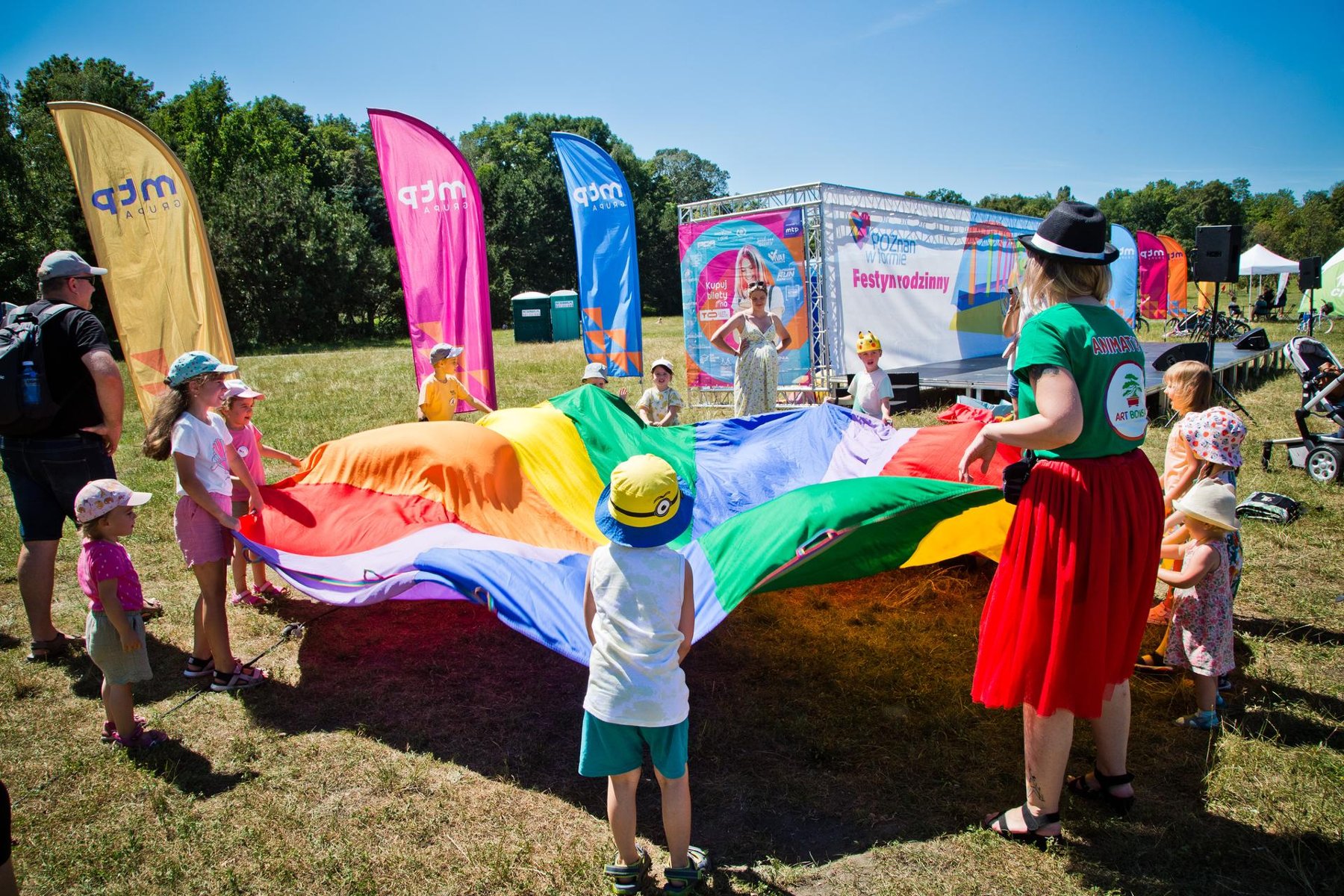 Na zdjęciu dzieci i animatorka bawiące się wielką, kolorową płachtą - grafika artykułu