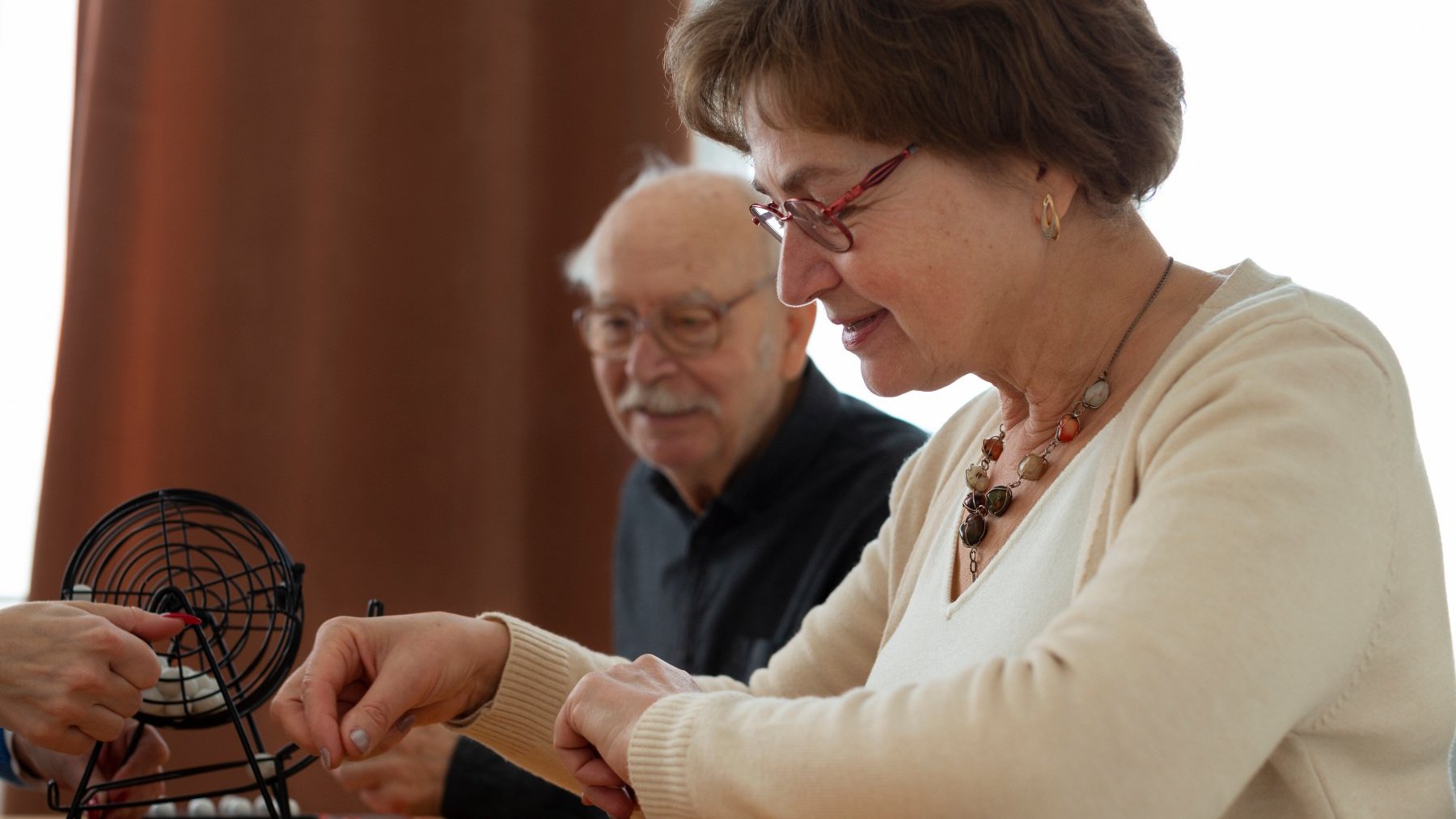 Na zdjęciu dwoje seniorów grających w grę planszową, na pierwszym planie kobieta, w tle mężczyzna