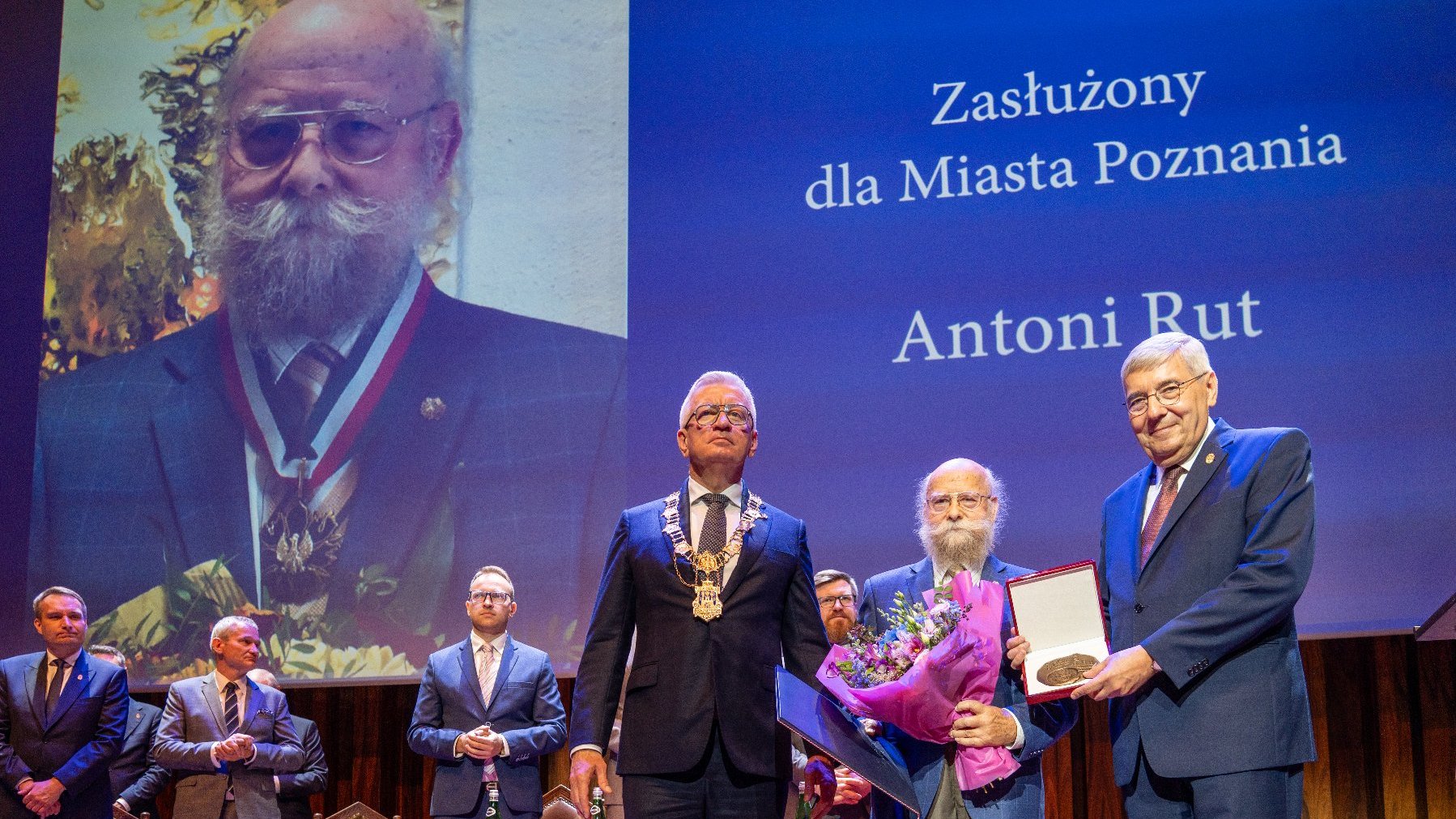 Na zdjeciu dwóch mężczyzn wręczajacych nagrodę trzeciemu
