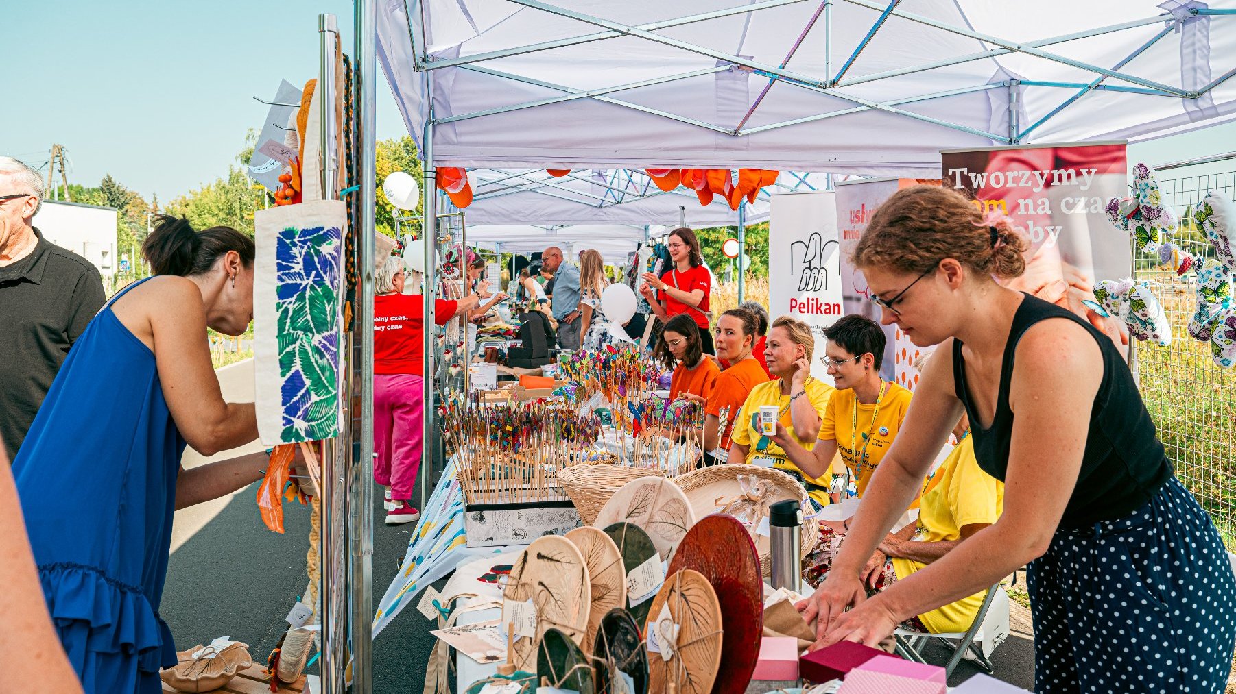 Na zdjęciu grupa ludzi przy stoiskach pod namiotami, na stoiskach rozłożone są różne przedmioty