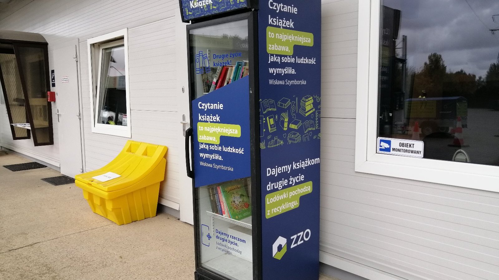 Zdjęcie przedstawia zamykaną półkę, przypominającą lodówkę, w której znajdują się książki.