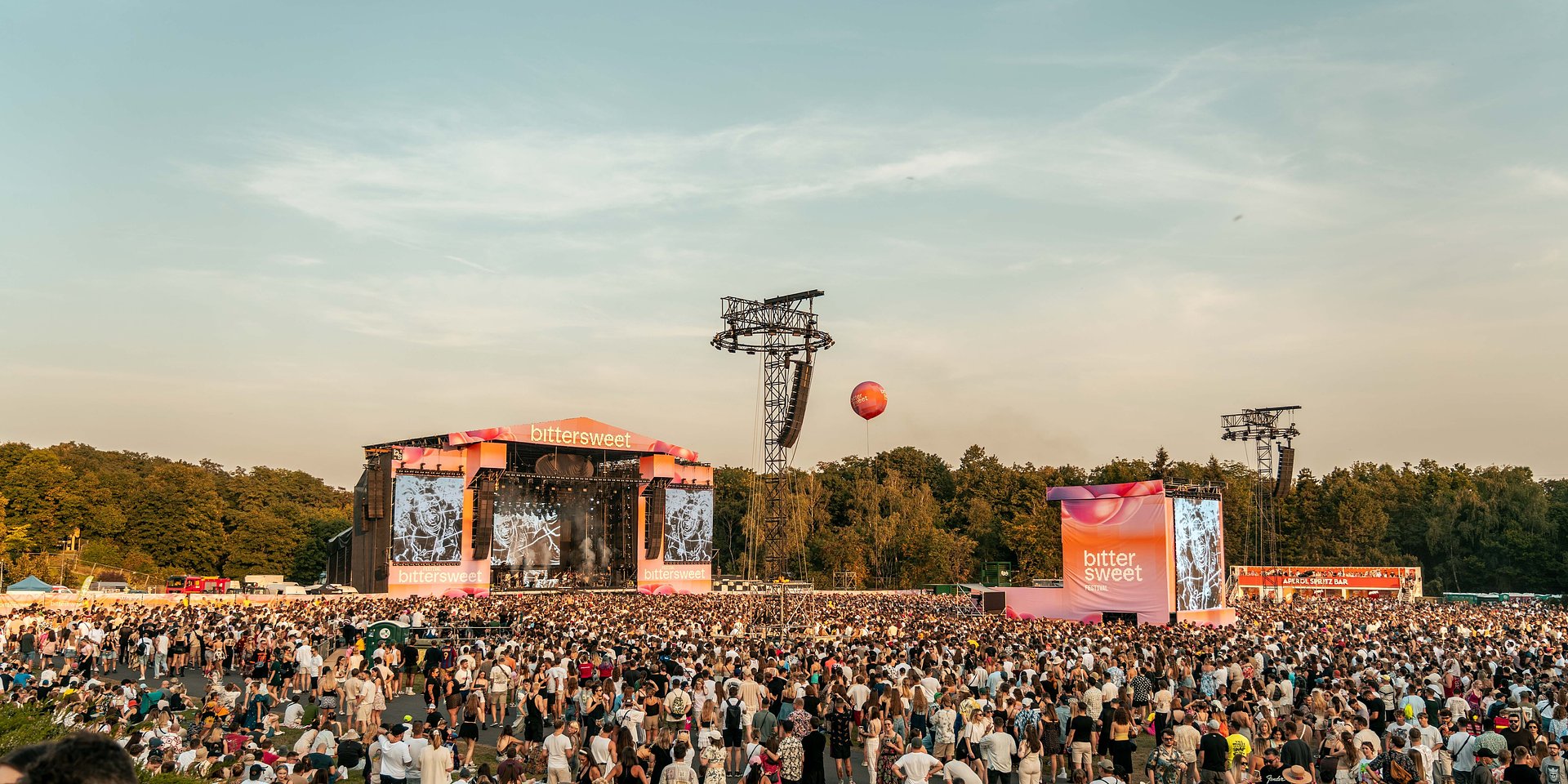 Na zdjęciu scena w otoczeniu zieleni, pod nią setki ludzi - grafika artykułu