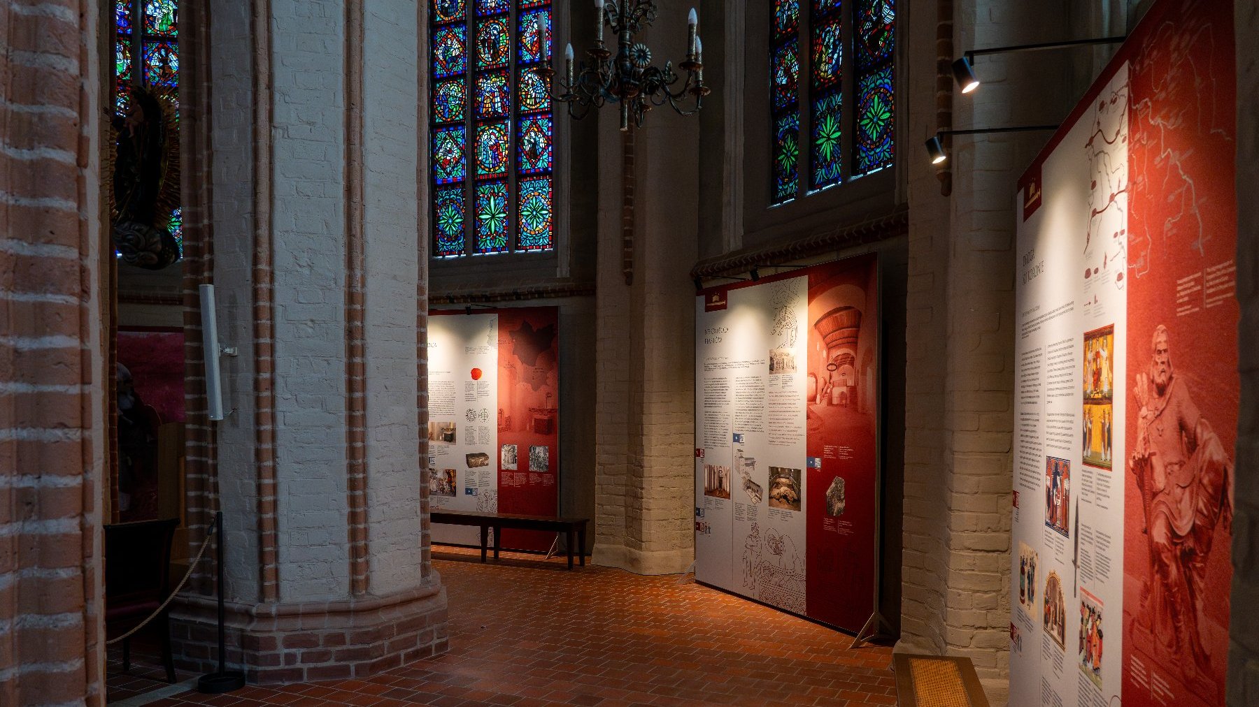 Zdjęcie przedstawia wnętrze kościoła z witrażami i elementami wystawy - plakatami z infromacjami i obrazkami.