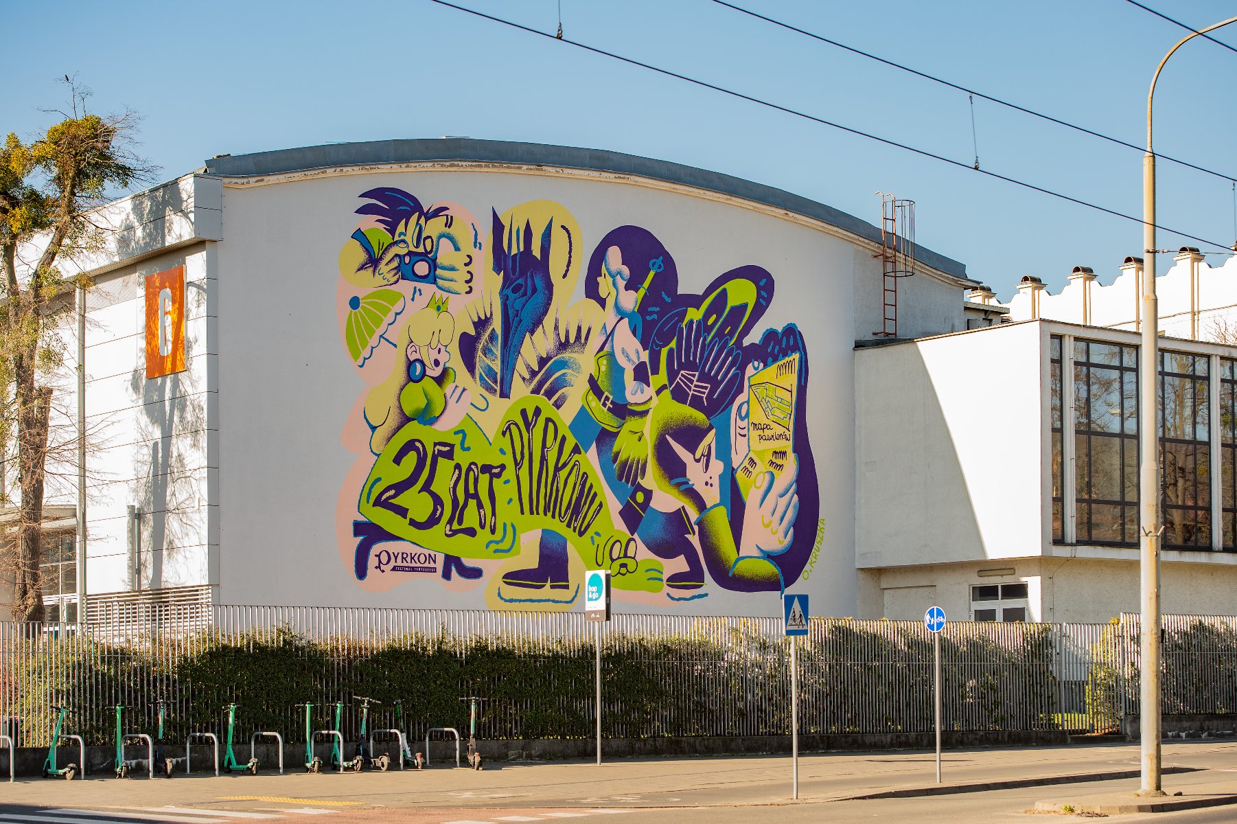 Wielki mural z wizerunkiem różnych fantastycznych postaci i napisem "25 lat Pyrkonu", umieszczony na ścianie jednego z budynków MTP. - grafika artykułu